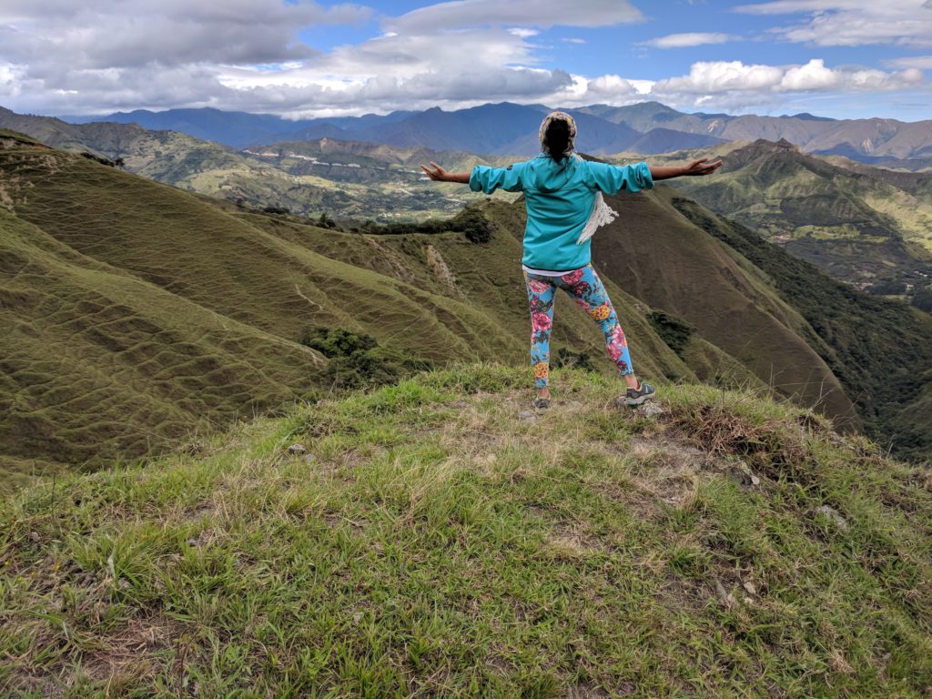 Ximena Morales Gamarra stands on mountain peak, arms outstretched, overlooking vast Andean landscape.